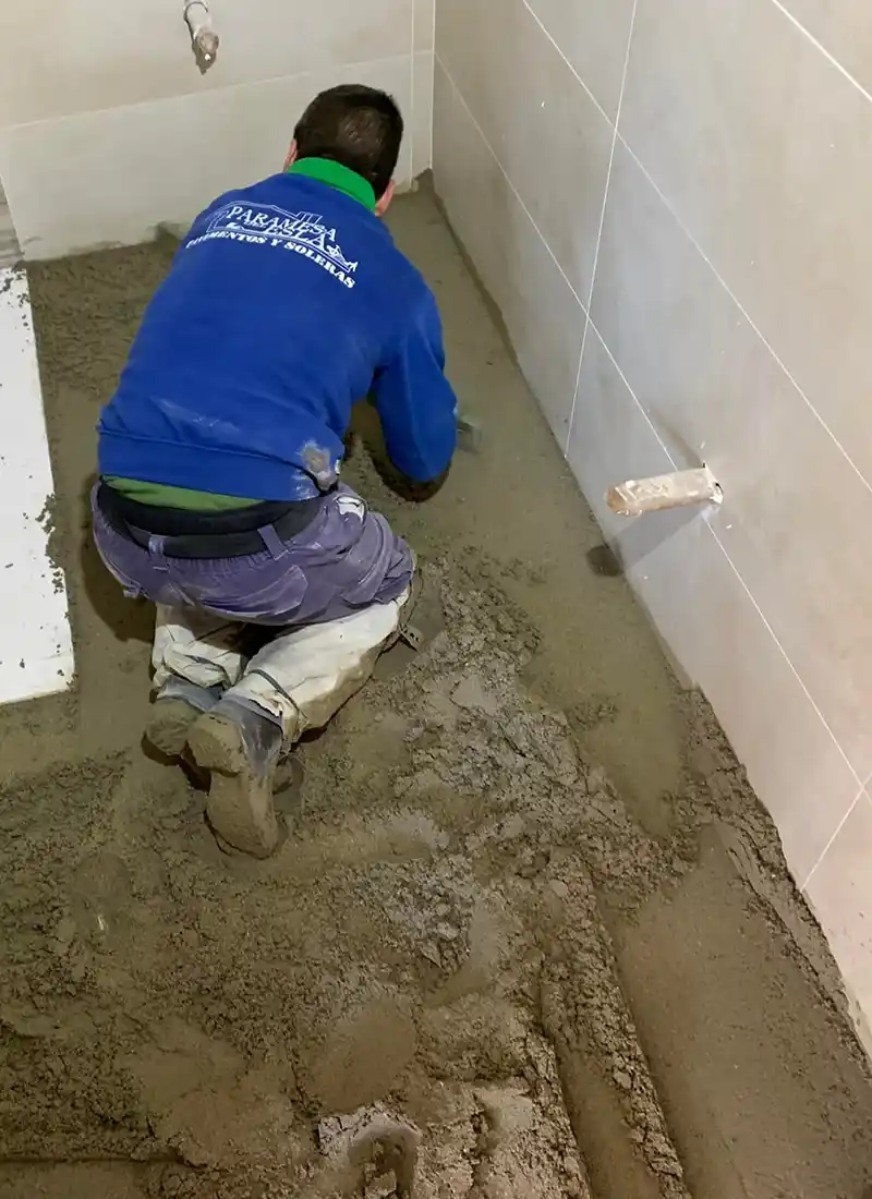 Trabajador echando solado de mortero en baño.